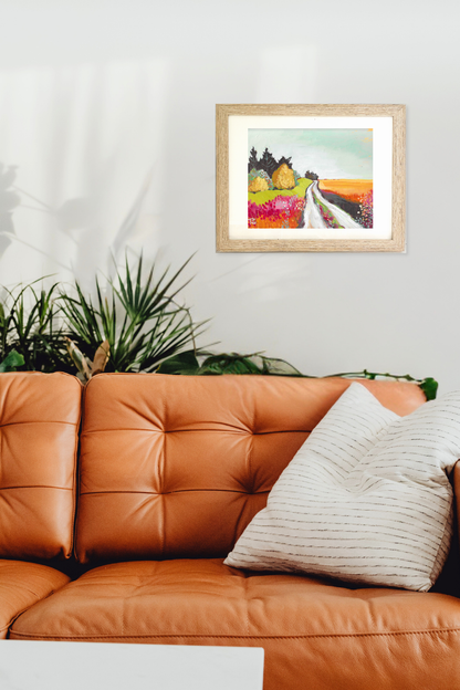 Framed artwork above an orange leather sofa with a plant in the background. Colorful landscape painting titled "Acre" by artist Teri Stephens