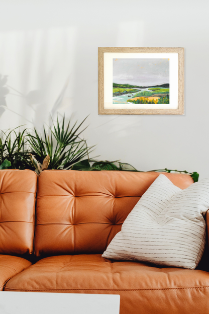 Framed landscape painting above a brown leather sofa with decorative pillows. "Brook" by Teri Stephens