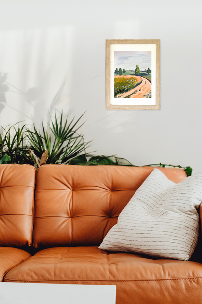 Framed landscape painting above a brown leather sofa with decorative pillows. Artwork titled Curve by Teri Stephens