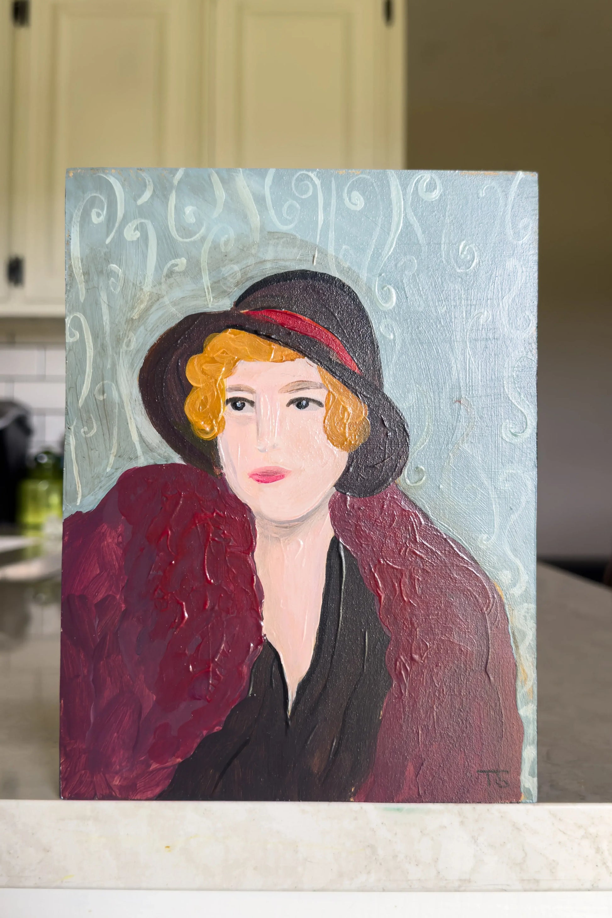 Painting of a woman wearing a black hat and red coat on a textured light blue background. Title: Della by Teri Stephens