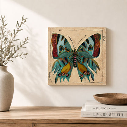A square wall art print featuring a colorful butterfly with teal, blue, yellow, and red wings on a beige background, displayed above a wooden console table with a vase, books, and a bowl in a styled interior setting.