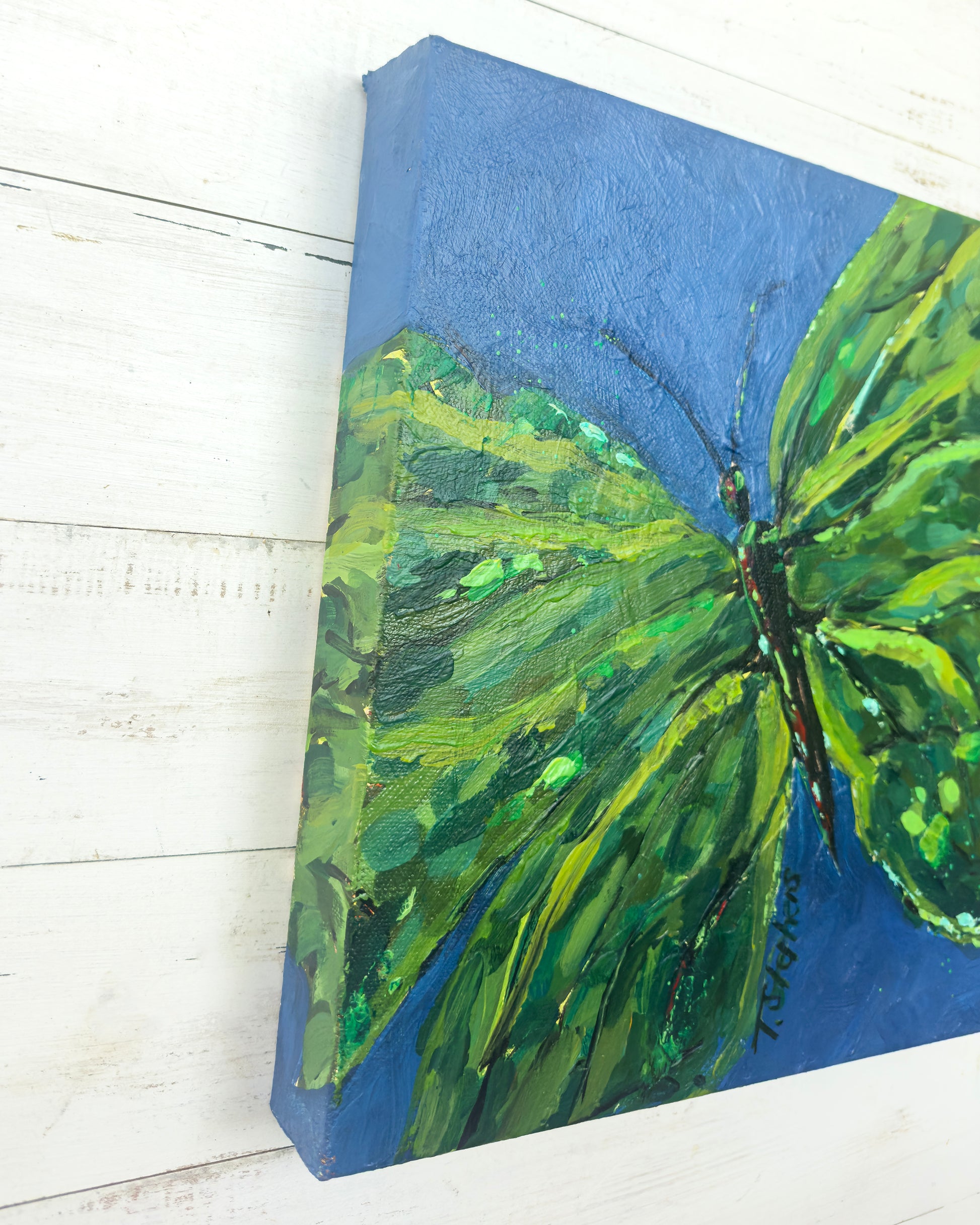 Painting of a green butterfly on a blue background, angled view of "Emerge", an original painting by Teri Stephens