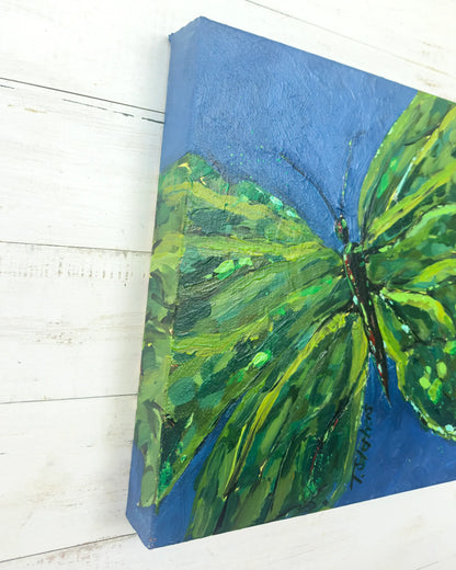 Painting of a green butterfly on a blue background, angled view of "Emerge", an original painting by Teri Stephens