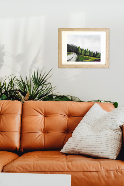 Framed landscape painting above an orange leather sofa with decorative pillows. Original artwork titled Evergreen by Teri Stephens