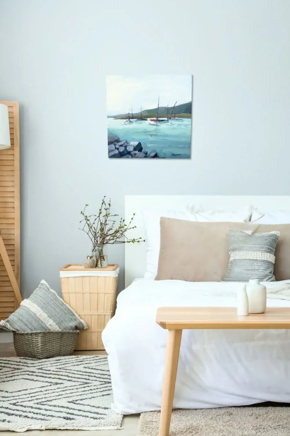 Cozy bedroom with a bed, table, and wall art of sailboats in a harbor. Original painting titled 'Harbor' by Teri Stephens