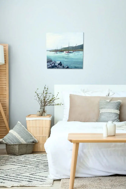 Cozy bedroom with a bed, table, and wall art of sailboats in a harbor. Original painting titled 'Harbor' by Teri Stephens