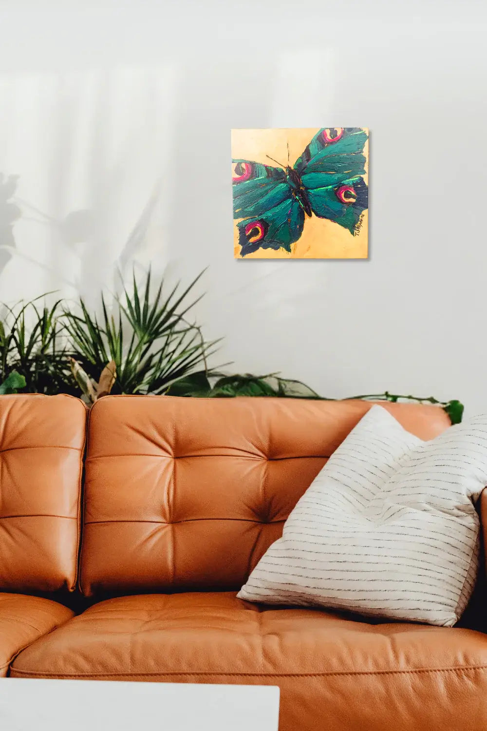 Orange sofa with a decorative pillow and a colorful butterfly painting on the wall, interior mock up featuring original painting "Jewel" by Teri Stephens