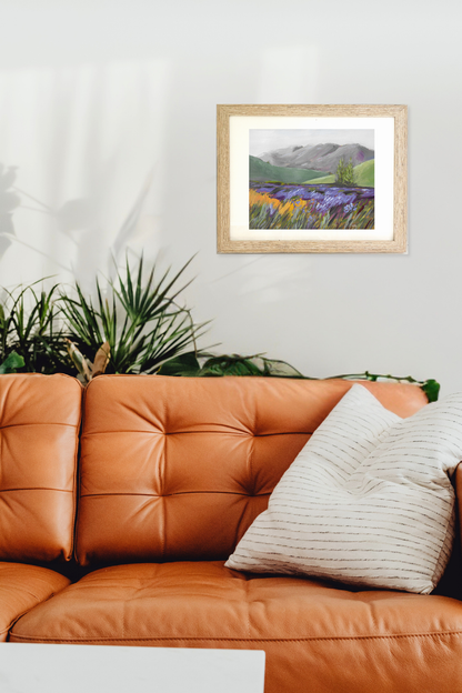 Framed landscape painting titled "Lavender" by artist Teri Stephens, above an orange leather sofa with a plant and pillow.