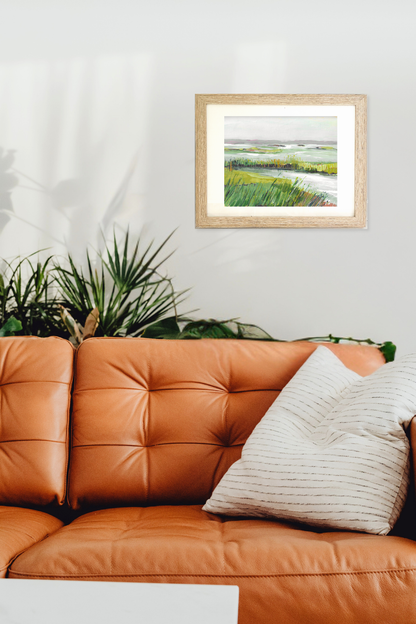 Framed artwork above an orange leather sofa with a plant in the background, coastal painting titled "Marsh" by artist Teri Stephens