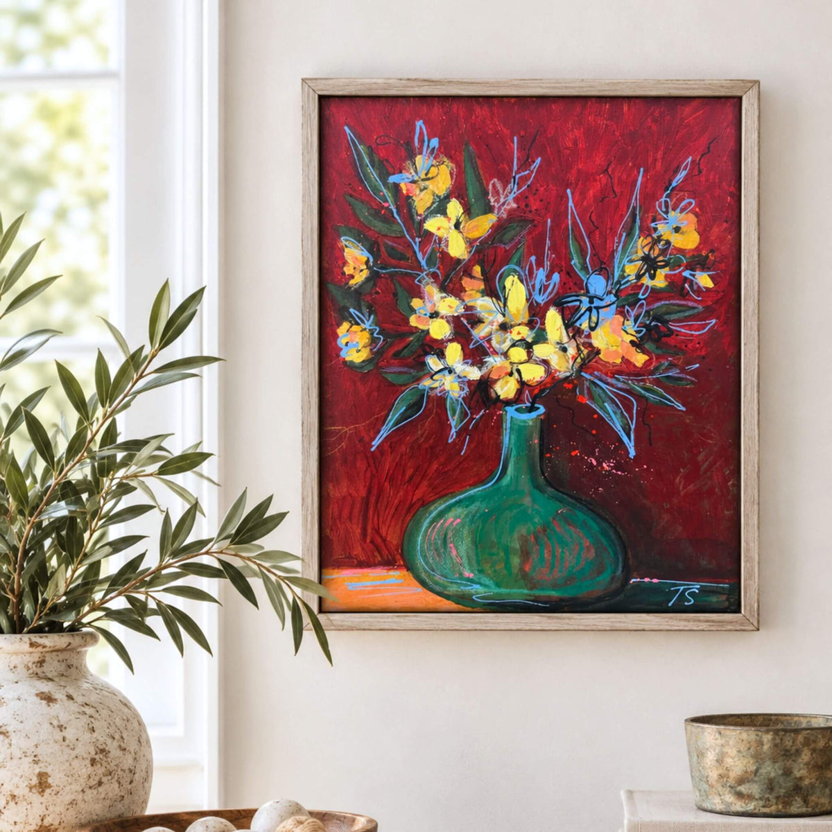 A framed painting of yellow flowers in a green vase against a textured red background, hanging on a light beige wall next to a window with a potted plant.