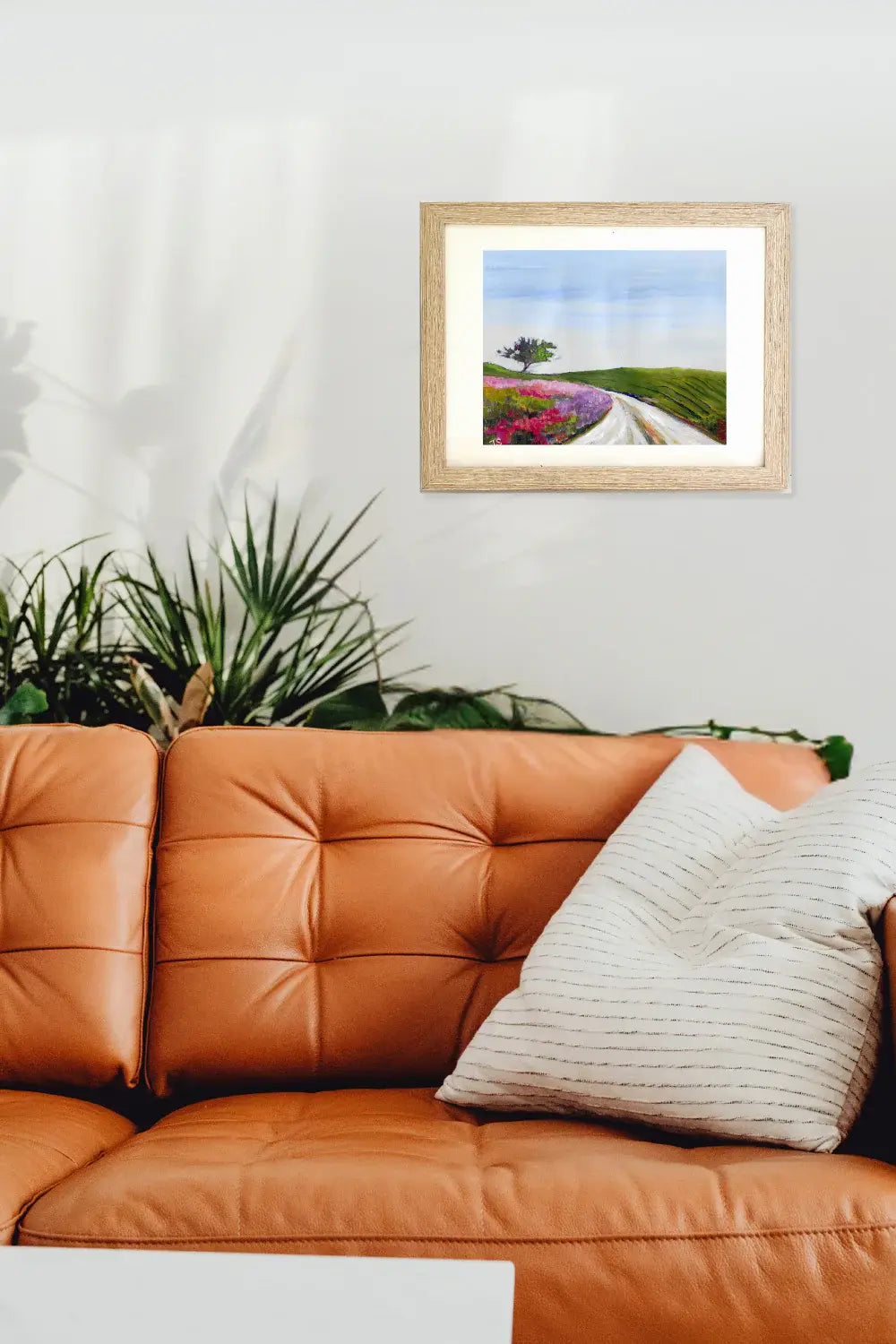Framed artwork of a landscape with a road and flowers on an orange couch.