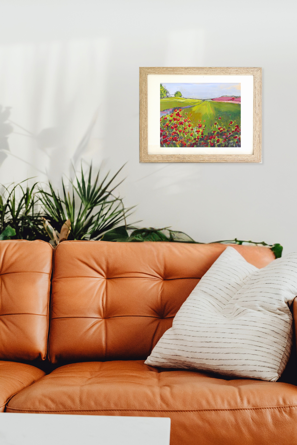 Framed artwork of a colorful landscape above an orange sofa with a plant in the background. Poppy by Teri Stephens