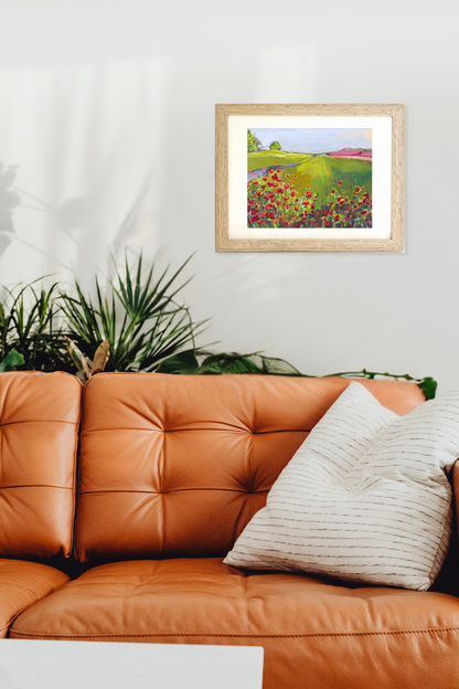 Framed artwork of a colorful landscape above an orange sofa with a plant in the background. Poppy by Teri Stephens