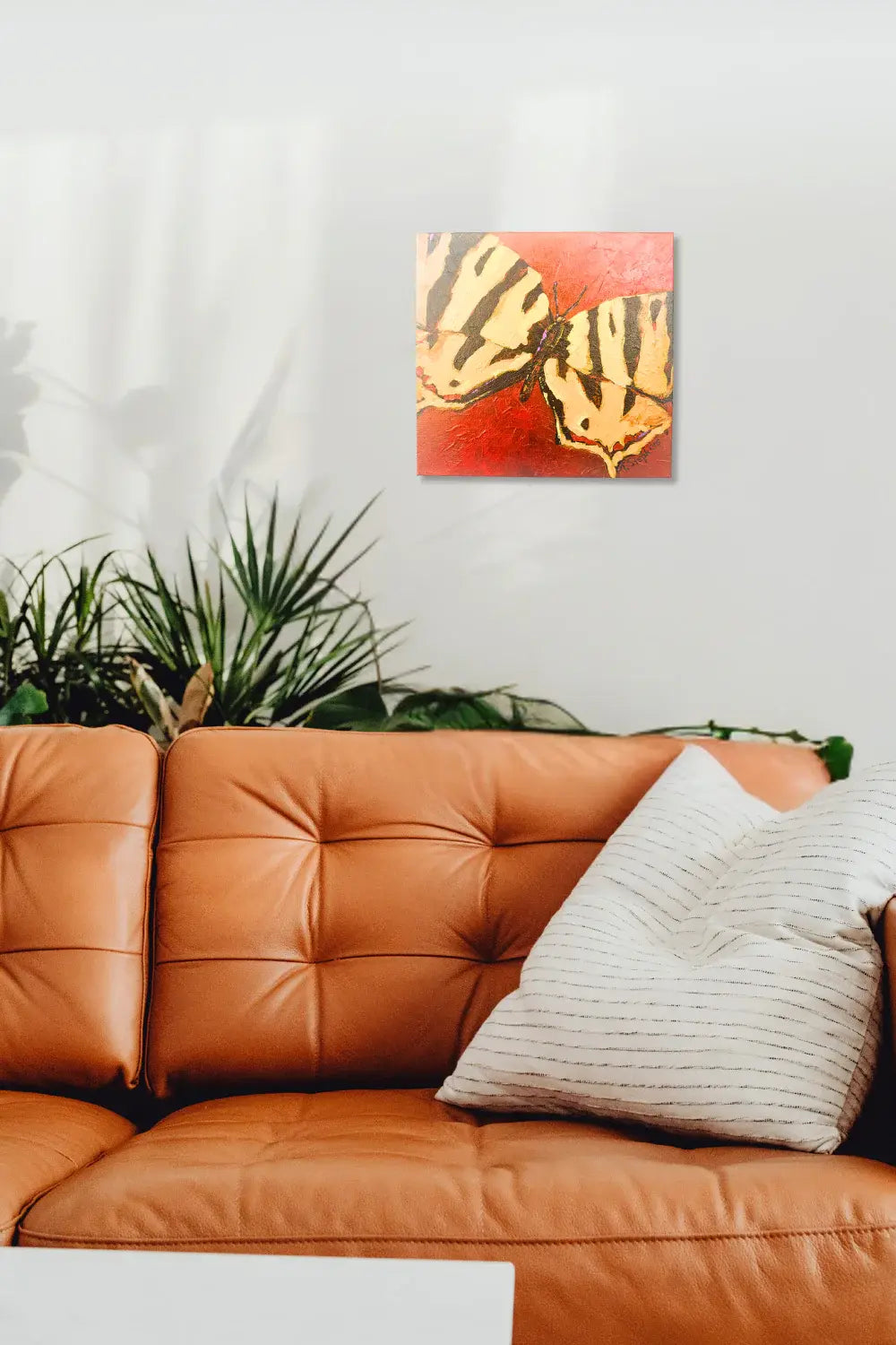 Orange leather sofa with a decorative pillow and a painting of butterfly wings on a red background. Interior  mock up featuring original artwork titled "Signal" by Teri Stephens