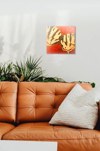 Orange leather sofa with a decorative pillow and a painting of butterfly wings on a red background. Interior  mock up featuring original artwork titled "Signal" by Teri Stephens