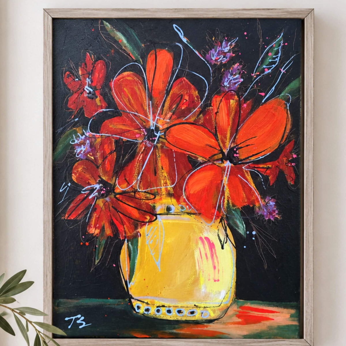 A framed painting of vibrant orange flowers in a yellow vase against a dark background, displayed on a light beige wall with a small plant leaf visible in the lower left corner. Titled "Somehow" by artist Teri Stephens