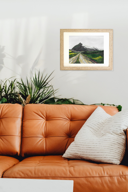 Framed landscape painting titled Summit by Teri Stephens on a wall above an orange sofa with decorative pillows.