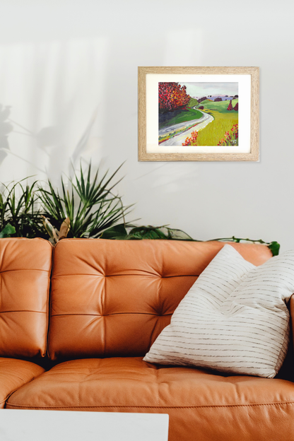 Framed artwork of a landscape titled Turf by artist Teri Stephens, on a wall above an orange sofa with a plant in the corner.