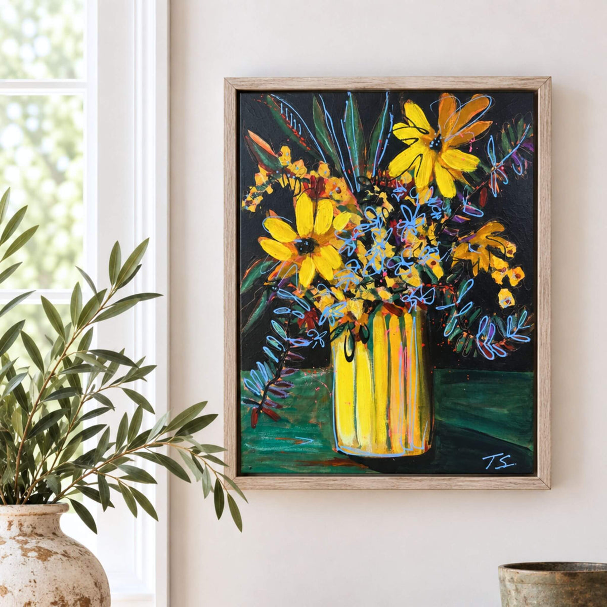 A framed painting of a vibrant yellow flower bouquet in a striped yellow vase, displayed on a light beige wall next to a potted green plant. Titled Until by artist Teri Stephens