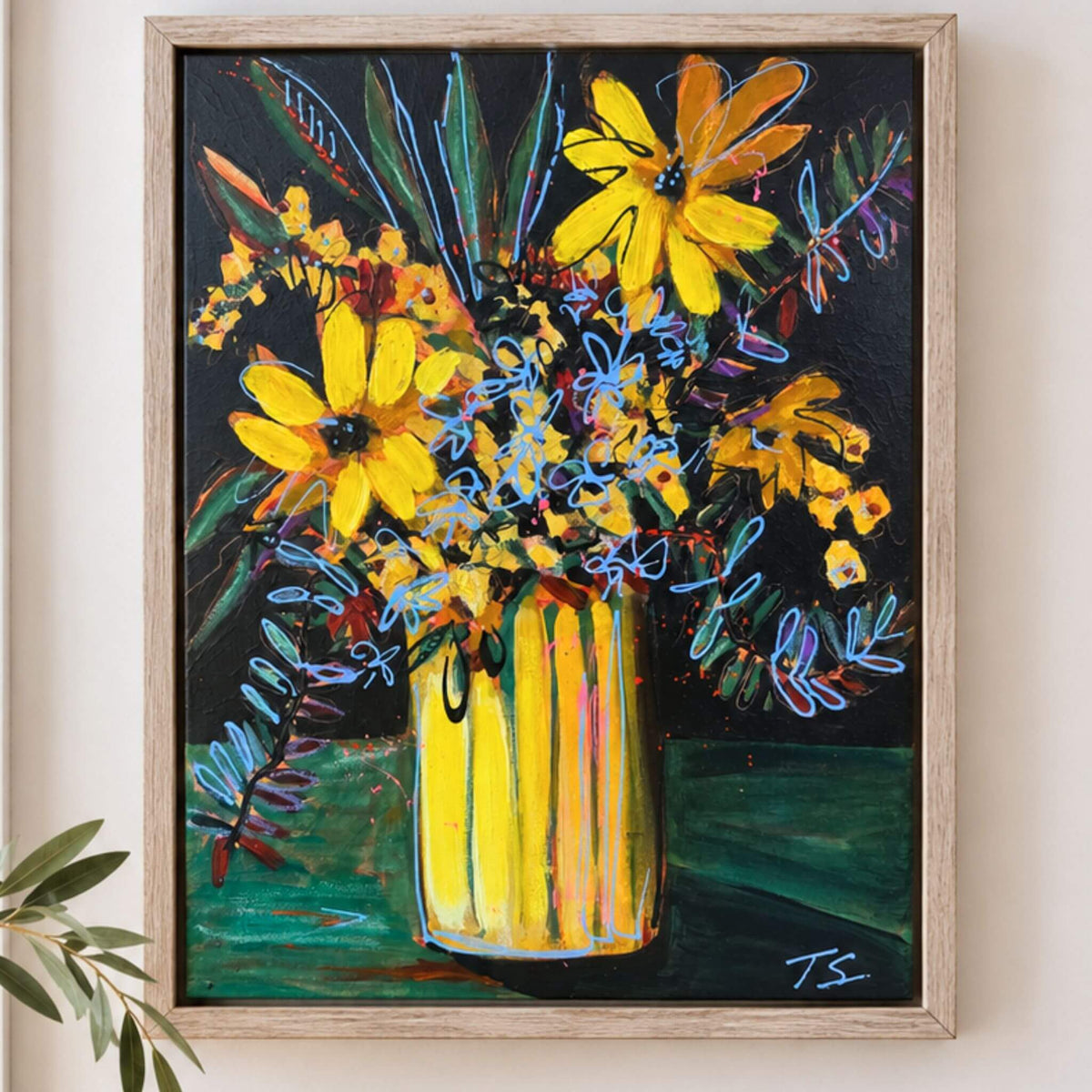 A framed painting of a vibrant yellow flower bouquet in a striped yellow vase against a dark background, displayed on a light beige wall with a small green plant leaf in the foreground.