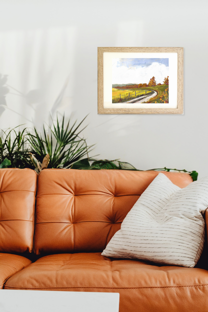 Framed landscape painting titled Vale by artist Teri Stephens, above an orange leather sofa with a plant in the corner.