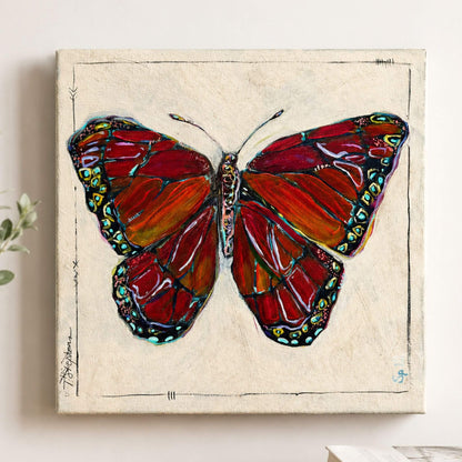 A square canvas wall art print featuring a stylized butterfly with red, orange, and black wings on a textured cream background, hanging on a light wall.